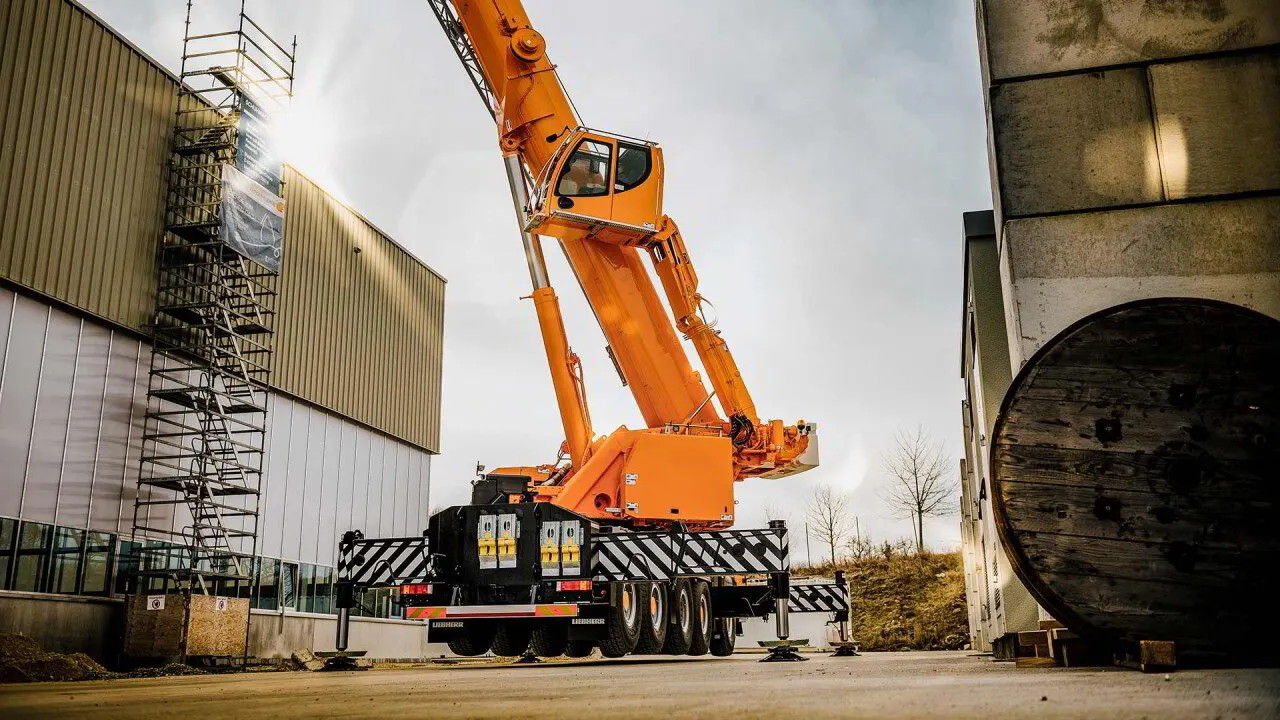 Orange all-terrain mobile crane with its boom raised beside an industrial building
