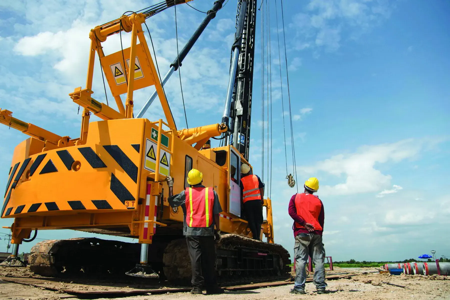 Three workers in hard hats and safety vests standing beside a yellow crawler crane on a job site