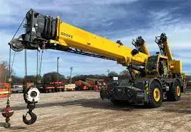 A yellow Grove rough-terrain crane with its boom retracted, parked in an equipment yard