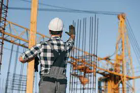 A worker in a hard hat raising his hand to signal a crane on a construction site