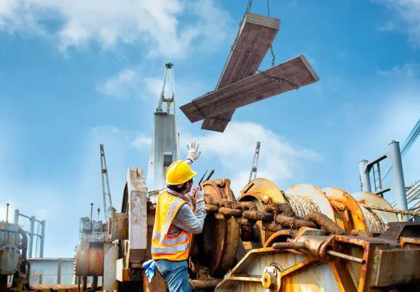 Worker in a hard hat signaling as a crane lifts a steel beam against a cloudy sky