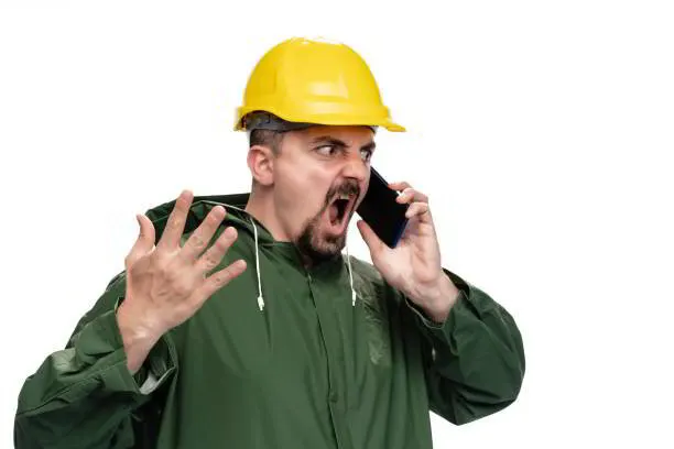 Frustrated worker in a yellow hard hat shouting into a phone