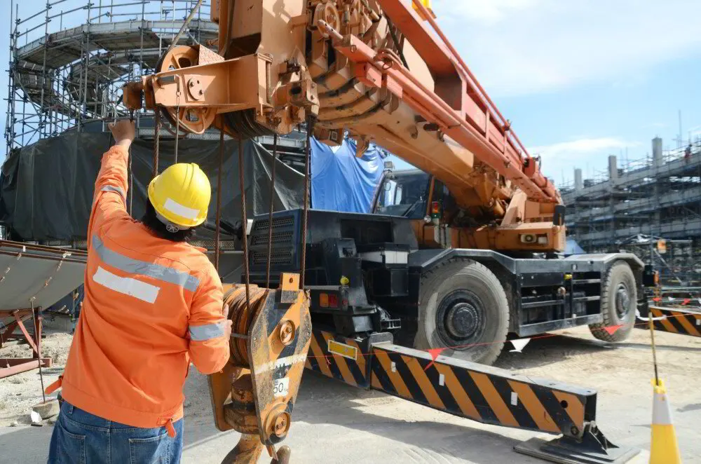 Rigger in a hard hat steadying a hook block beneath a mobile crane