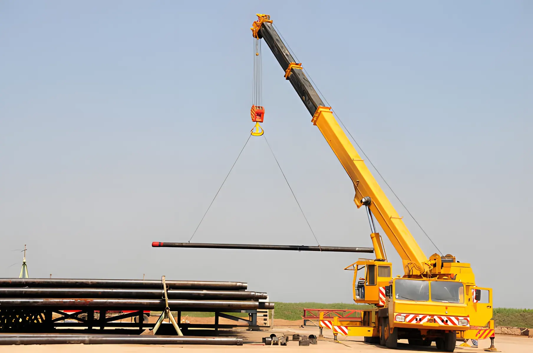 Yellow mobile crane with its boom raised lifting a load in an open yard