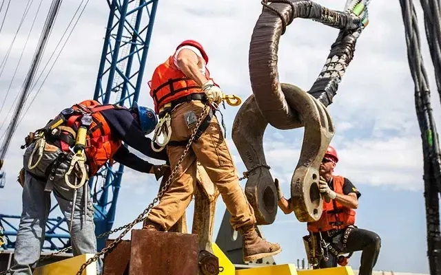 Riggers in safety harnesses attaching a large shackle to a crane load